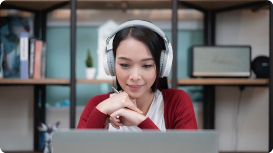 photo of asian woman in red sweater wearing white headphones and looking at a laptop