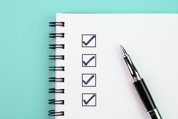 Hire Skilled Back Office Staff in 7 Days A spiral notebook with four checked boxes on a checklist page and a black pen on the right side, all set against a light blue background—perfect for organizing tasks as you Hire Skilled Back Office Staff in 7 Days.